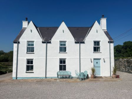 A house with a front door and patio furniture at Cae Du Dwyran near Niwbwrch (Newborough)