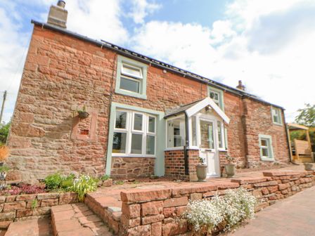 A stone exterior of a house with a white porch and plants in pots at Rock Cottage in Penrith