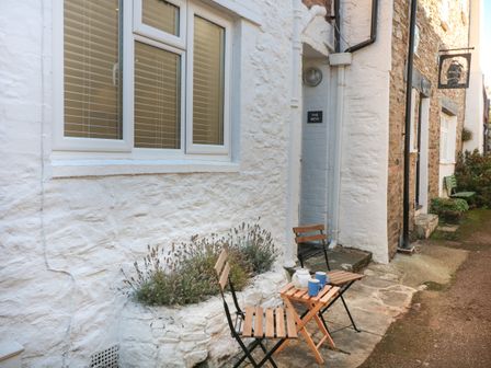 An outdoor seating area with wooden chairs and a small table holding a teapot and mugs outside a white stone building at The Mew in Dartmouth
