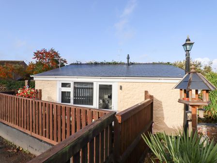 A small single-story building with beige walls and a dark roof behind a wooden fence at The Park Inn Piggery in Kingskerswell