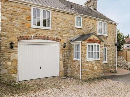 Exterior view of a stone house with white framed windows a white garage door and a small porch at Fisherbridge Cottage Weymouth