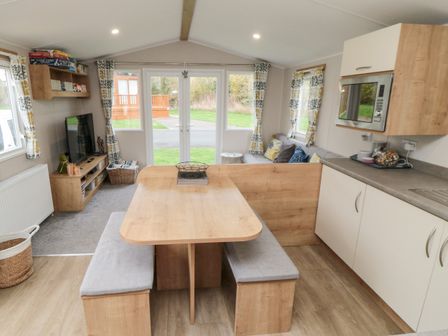A dining area with wooden table and bench seats next to a kitchen and living room at Pines 30 in Cayton