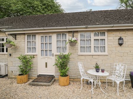 A stone exterior wall with a white door and windows a small white table with two chairs and plants outside at Paddock Cottage Nr Malmesbury