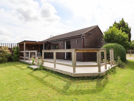 A wooden cabin with a deck and garden surrounding it at Meols Holiday Lodge in Meols