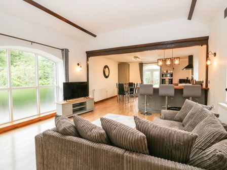 A living room with a grey sofa a television on a cabinet and an open kitchen with bar stools at Coach House in Arnside