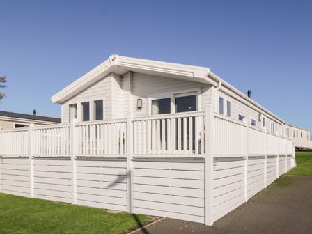 A white mobile home with a white fenced deck on a grassy area at Dershel Lodge in Southerness