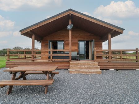 A wooden cabin with a small porch and picnic table in front at The Lodge at Crossroads Farm in Middlezoy