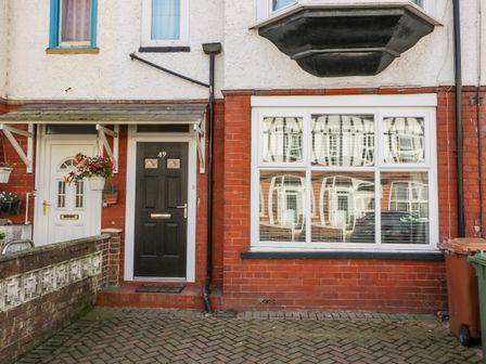 Front doors and windows of a brick house with hanging flower pots and trash bins at Cosy Coastal Holiday Let in Bridlington