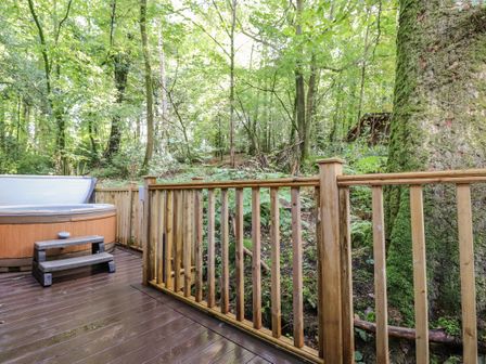 A wooden deck with a hot tub and steps next to a railing overlooking a forest at Woodland Retreat Skiptory Howe 41A White Cross Bay near Windermere