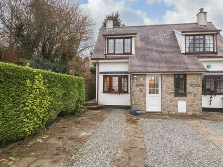 A stone and white exterior semi detached house with gravel driveway and trimmed hedge at Craig Mawr in Benllech