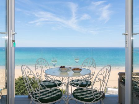 A balcony with a round table and four chairs overlooking the beach and ocean at Surf and Sand in Carbis Bay
