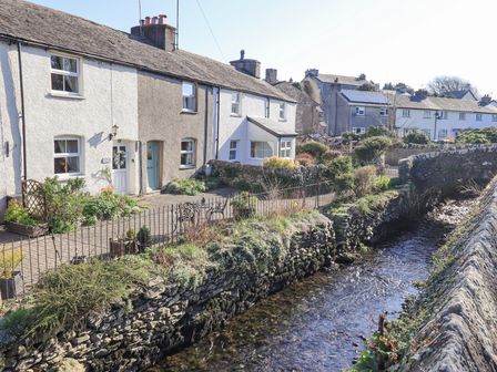 A row of terraced houses along a stone-lined stream with a small stone bridge at Lavender Cottage in Cark In Cartmel