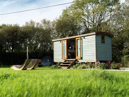 A small wooden cabin with open doors on a grassy lawn with two wooden lounge chairs and trees in the background at Fern in Broad Langdon near Wainhouse Corner