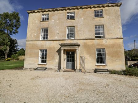 A large stone house with six windows and a central door with columns at Rockstowes House Uley near Dursley