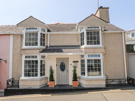 A two story house with bay windows and a central door with plants in pots at Bodwena in Moelfre