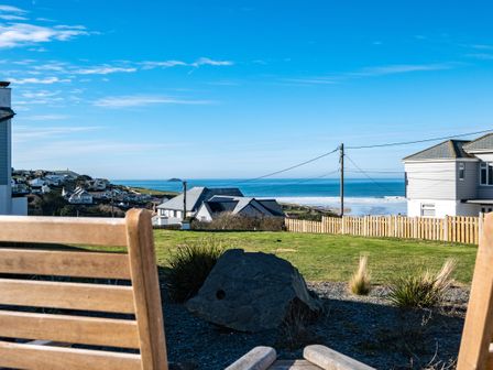 A coastal view with houses a grassy area a wooden fence and chairs overlooking the sea at Blue Ridge in Polzeath