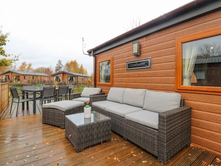 An outdoor seating area with wicker furniture and a dining table on a wooden deck at Clearwater in Warton near Carnforth