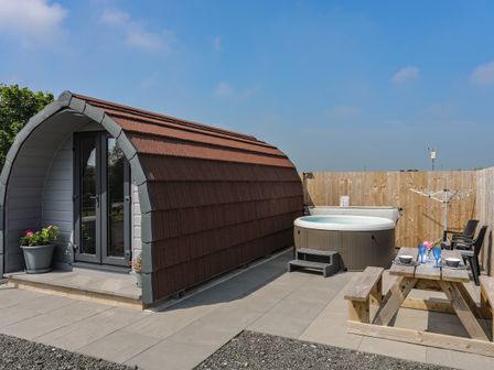 An outdoor area with a small pod structure a hot tub a wooden picnic table and chairs at Parys Pod in Amlwch