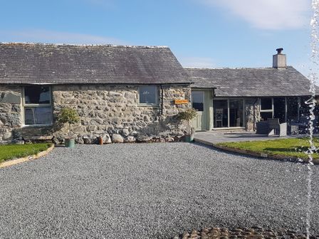 A stone building with a gravel driveway and small trees in pots at Y Bwthyn in Dyffryn Ardudwy