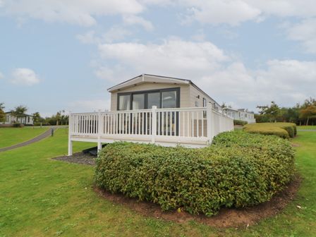 A mobile home with a white fence and bushes in front on a green lawn at 10 Cheviot View in Haggerston near Lowick