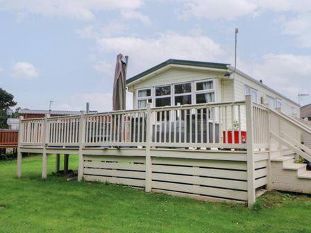 A raised deck with a railing and stairs attached to a small white house with multiple windows on a grassy lawn at Hedgehog Retreat in Felton