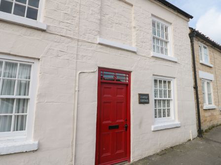 A red front door with windows on either side on a stone cottage called Castle Cottage at 12 Castlegate in Pickering