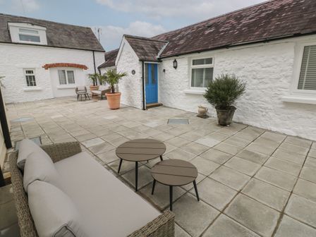 An outdoor patio with stone tiles two round tables a sofa potted plants and white buildings with a blue door at Bluebell Cottage Jameston near Manorbier