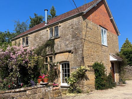 A stone cottage with climbing plants flowers and potted plants outside at Ham cottage in East Lambrook near South Petherton