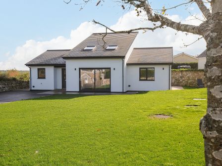 A modern house with white walls and a gray roof surrounded by grass and a tree branch in the foreground at Zephyr in Gweek