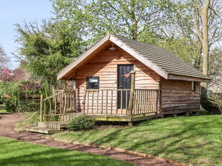 A wooden cabin with a small porch and steps surrounded by grass and trees at Pheasant in Bedale