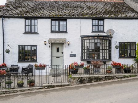 A white building with black windows and a patio with tables and flowers at Church View Cottage Near Looe