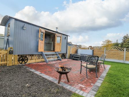 An outdoor patio with a fire pit two chairs a wooden fence and a gray caravan with open doors at Poppy in St Harmon near Rhayader