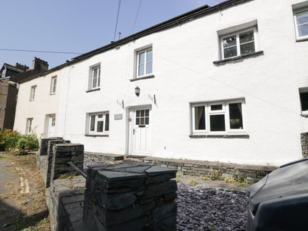 A white stone cottage with multiple windows and a stone wall in front at Taylors Cottage in Threlkeld near Keswick