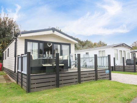 A mobile home with outdoor seating area and glass doors on a grassy plot at 3 Yealands in Carnforth
