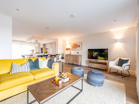A living room with a yellow sofa blue poufs wooden coffee table and a television at Porth Beach Villa in Porth near Newquay