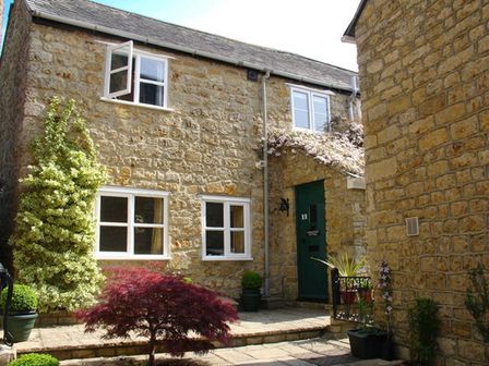 Stone house exterior with green door and windows surrounded by plants and small trees at Fiddlesticks Cottage in Beaminster
