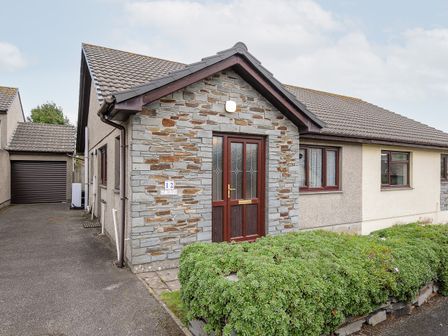 A single-story house with a stone entrance porch a wooden door and surrounding shrubs at St Albans in Boscastle