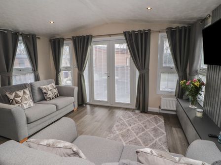 A living room with sofas pillows curtains a rug flowers on a table and a television at 24 Sherwood in Carnforth
