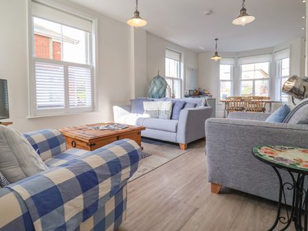 A living room with sofas a wooden coffee table and a dining table with wooden chairs at Seas The Day in Southwold
