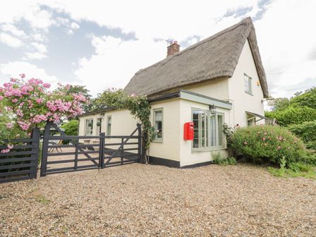 A cottage with a thatched roof and a black wooden gate surrounded by pink flowering plants at Waveney Cottage in Weybread near Harleston