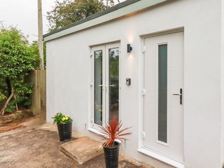 An entrance area with a white door and glass double doors with two potted plants outside at Pheasant View in Penelewey near Carnon Downs