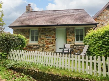 A stone cottage with a patio table and two chairs behind a white picket fence at Ty Rhydd in Newport Pembrokeshire