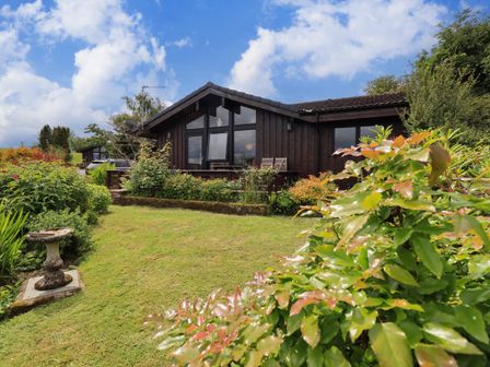 A garden with plants a birdbath and a wooden house with large windows at Greengarth Yanwath near Penrith