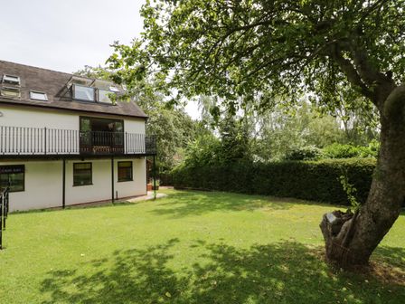 A backyard with grass a tree and a two story house with a balcony at Hillcroft in Burton Green near Kenilworth