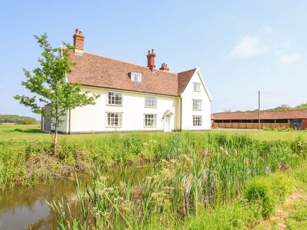 A white two-story house with a brown tiled roof near a pond and grassy field at South Grange House - Sleeps 12 in Sibton