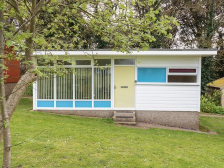 A small single-story building with a yellow door blue and purple panels and vertical window blinds at 107 Kings Chalet Park in Cromer