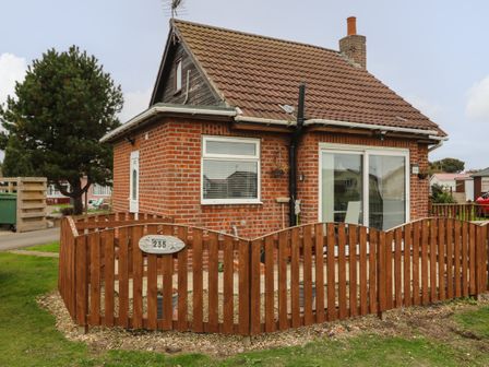 A brick house with a brown tiled roof and wooden fence in a grassy area at Chalet 235 Wilsthorpe near Bridlington