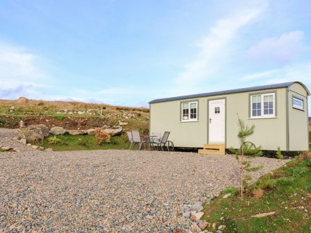 A small green mobile home with white door and windows on a gravel area with outdoor chairs and table at Shepherds Retreat Glenlark in Gortin near Greencastle
