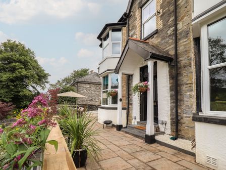 An exterior view of a stone and brick house with a paved patio area and potted plants at Bron Celyn in Betws-Y-Coed