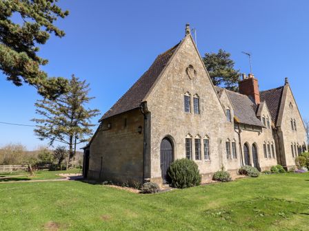 An old stone building with arched windows and doors surrounded by green grass and trees at The Alms House West in Tewkesbury